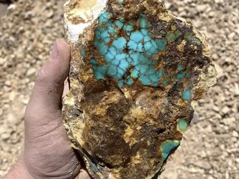 A hand holding a rock specimen with bright blue turquoise.