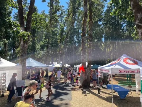 People walking along a path lined with trees and vendor tents during an outdoor event.