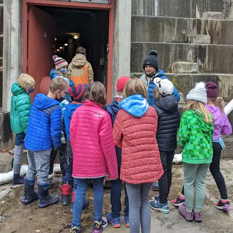 A group of children and an adult stand outside an open doorway.