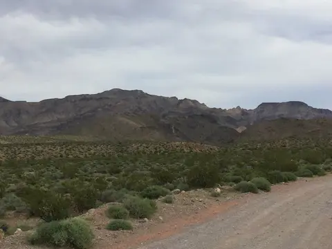 A dirt road running through a desert landscape with distant mountains under a cloudy sky.
