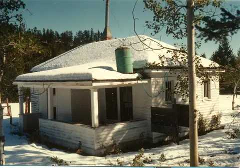A small white building with a snow-covered roof sits in a snowy landscape.