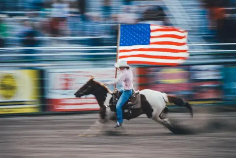 A person rides a horse while carrying an American flag.