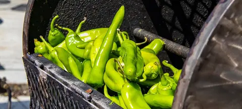 Green peppers roasting in a metal roaster.