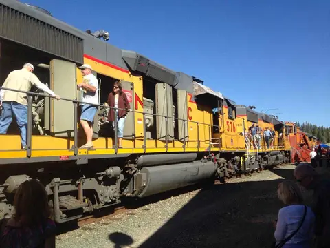 People stand on and around a yellow diesel locomotive train.