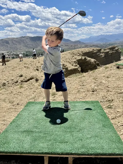 A young boy swings a golf club on an outdoor driving range.