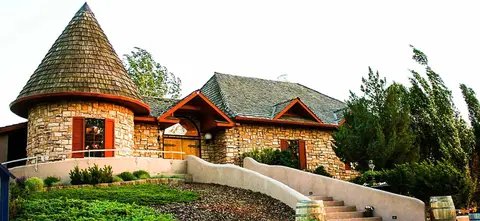 Exterior view of a stone building with a conical shingled tower and curved entrance stairs.