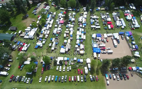 An aerial view shows an outdoor market with numerous tents and parked vehicles.