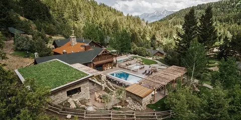 An aerial view of a resort lodge with swimming pools nestled in a mountain valley.
