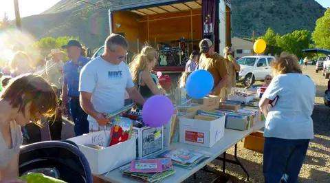 A crowd gathers around tables with books at an outdoor event.