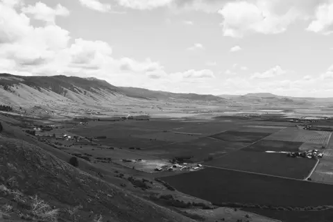 A black and white wide-angle photograph of a valley surrounded by mountains.
