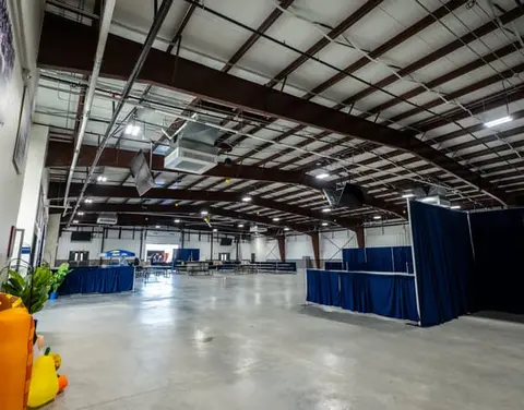An interior view of a large warehouse or event space with exposed steel beams and concrete floors.