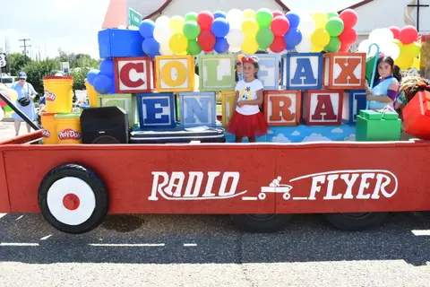 A parade float decorated as a giant red Radio Flyer wagon with children on it.