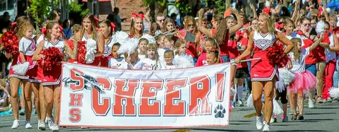 A group of cheerleaders carries a banner in a parade.