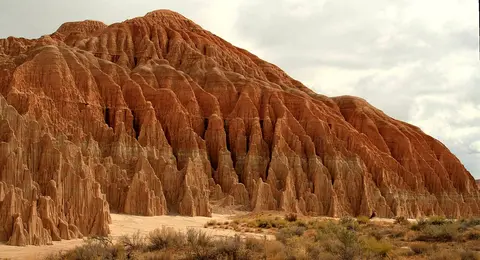 A landscape photo of a large eroded red rock formation with spires.