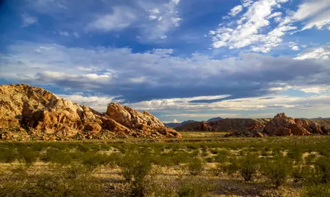 A landscape showing desert mountains and a cloudy blue sky.