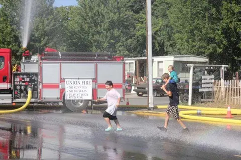 Children play in the water sprayed from a fire truck.