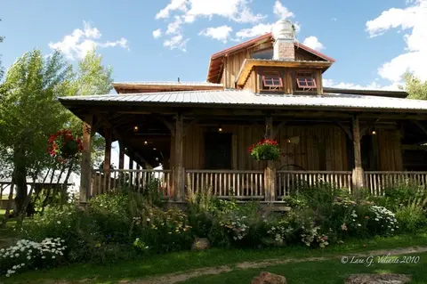 A wooden rustic building with a covered porch and surrounding garden.