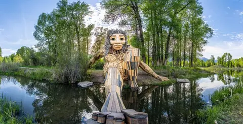 A large wooden sculpture of a troll sits near a body of water.