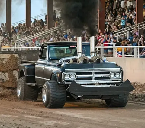 A modified truck participates in a tractor pull event in front of a crowd.