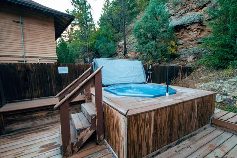 A hot tub on a wooden deck outside a building near a rocky slope.