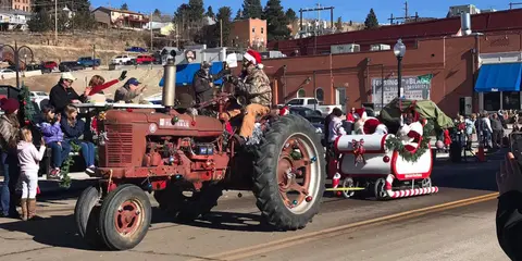 A decorated tractor pulling a float with people in a holiday parade.