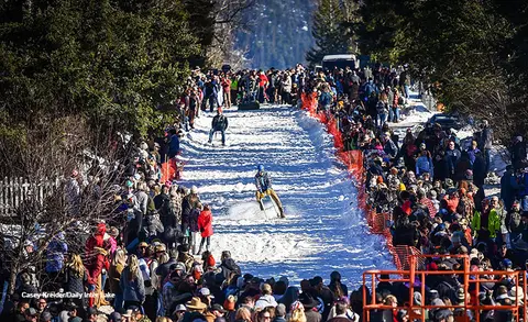 A person riding a bicycle down a snow-covered road lined with a large crowd of spectators.