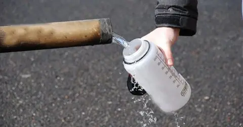A person filling a water bottle from a pipe.