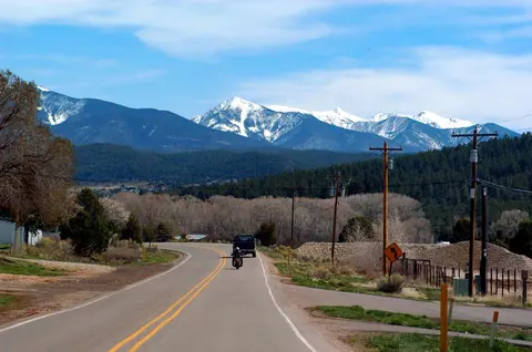 A winding road leads toward snow-capped mountains under a blue sky.