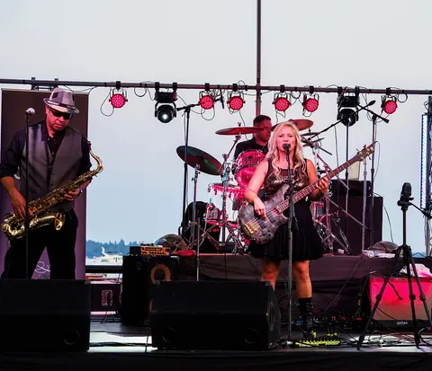 A band performs on an outdoor stage with lighting equipment.