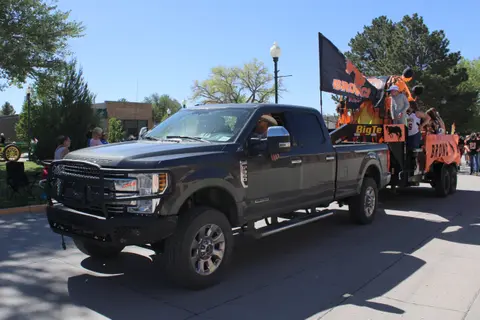 A dark pickup truck tows a decorated parade float along a sunny street.