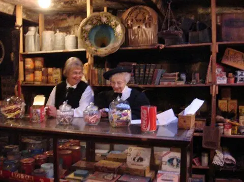 Two women behind the counter in a historic store with shelves of merchandise.