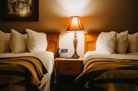 A photograph showing two beds with a nightstand and lamp between them.