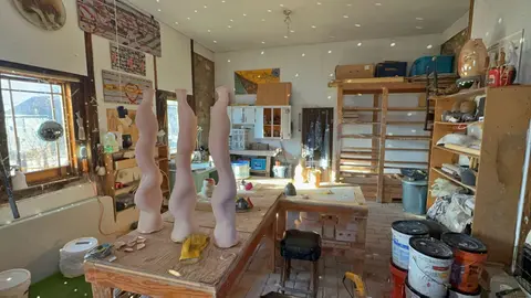 An artist's studio interior shows several tall, curved ceramic sculptures on a work table.