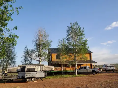 A two-story log cabin with a pop-up camper and pickup trucks parked outside.