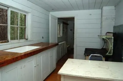 An interior view of a rustic kitchen with white wooden walls and a wooden countertop with a sink.