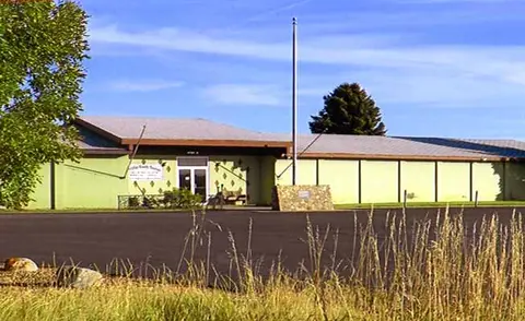 An exterior view of a single-story building with a flagpole in front.