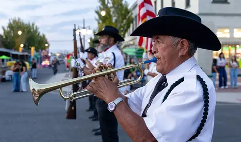 A man in a white uniform and cowboy hat plays a trumpet in a parade.