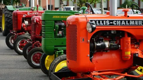 A row of vintage tractors is parked outdoors.
