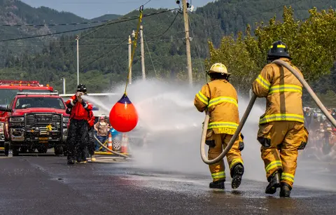Firefighters spray water at a hanging target during an outdoor event.