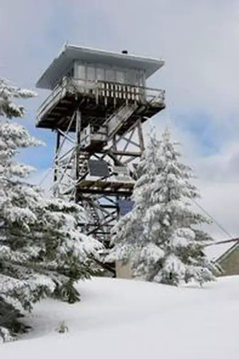 A tall wooden fire lookout tower surrounded by snow-covered pine trees.