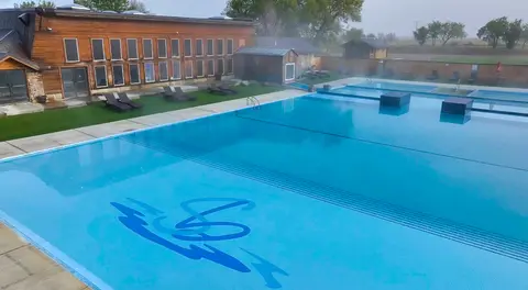 A large swimming pool sits beside a wooden building with many windows.