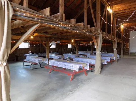 An interior view of a rustic wooden barn decorated with tables and string lights for an event.