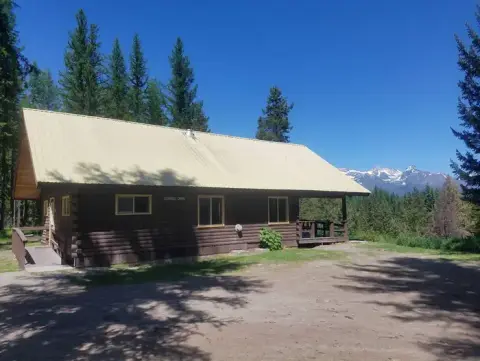 A log cabin with a metal roof surrounded by trees and mountains.