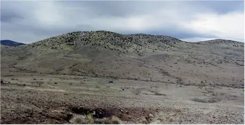 A wide view of dry rolling hills and sparse vegetation under a cloudy sky.