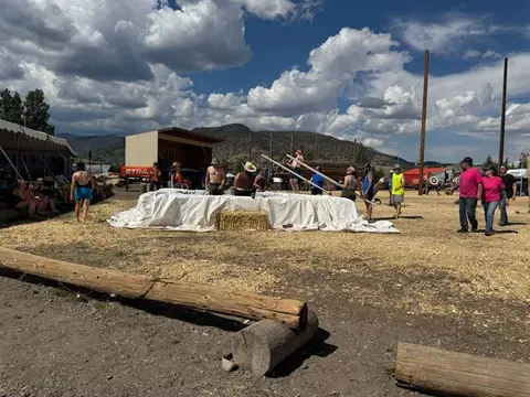 An outdoor gathering with people near a covered pool and logs under a cloudy sky.