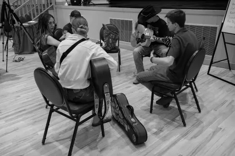 A group of people sitting in a circle playing acoustic guitars indoors.