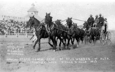 Historic black and white photograph of a horse-drawn stagecoach at an event.