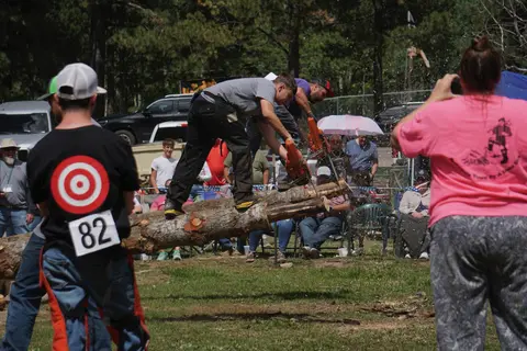 A competitor cuts a log with a chainsaw during an outdoor lumberjack event.