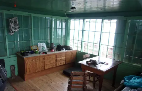 An interior view of a rustic room with wooden floors, green walls and cabinetry, and multiple windows.