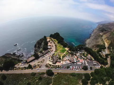 An aerial view shows a coastal landscape with buildings and parking lots next to the ocean.